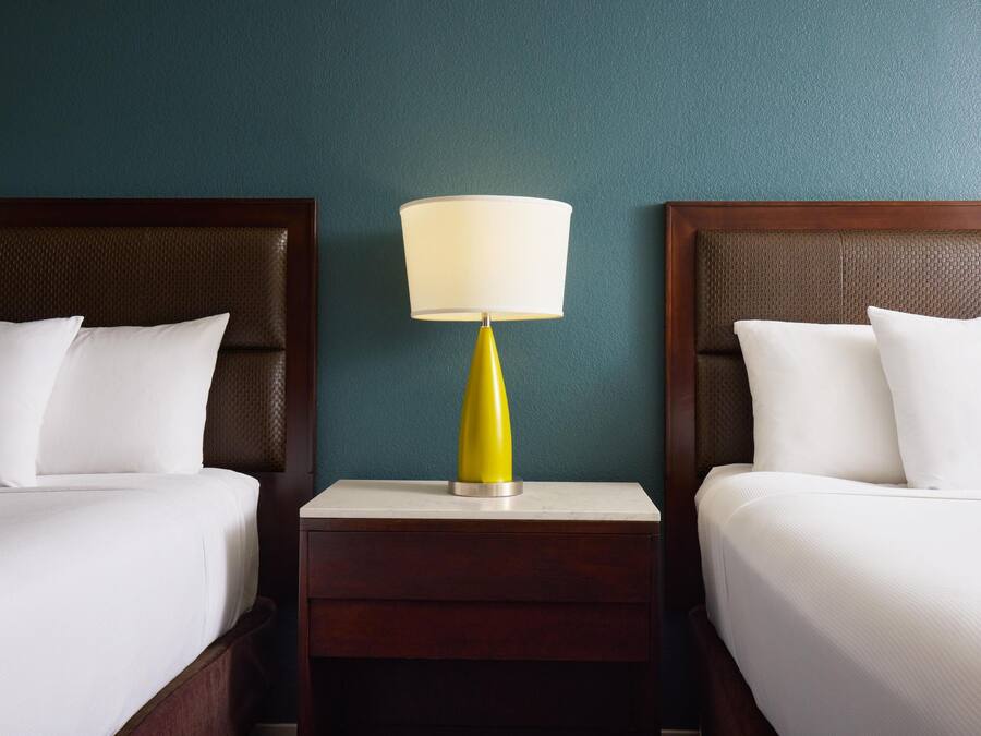 Ein Hotelzimmer mit zwei Betten, einem Nachttisch mit Lampe und teal-farbenen Wänden.