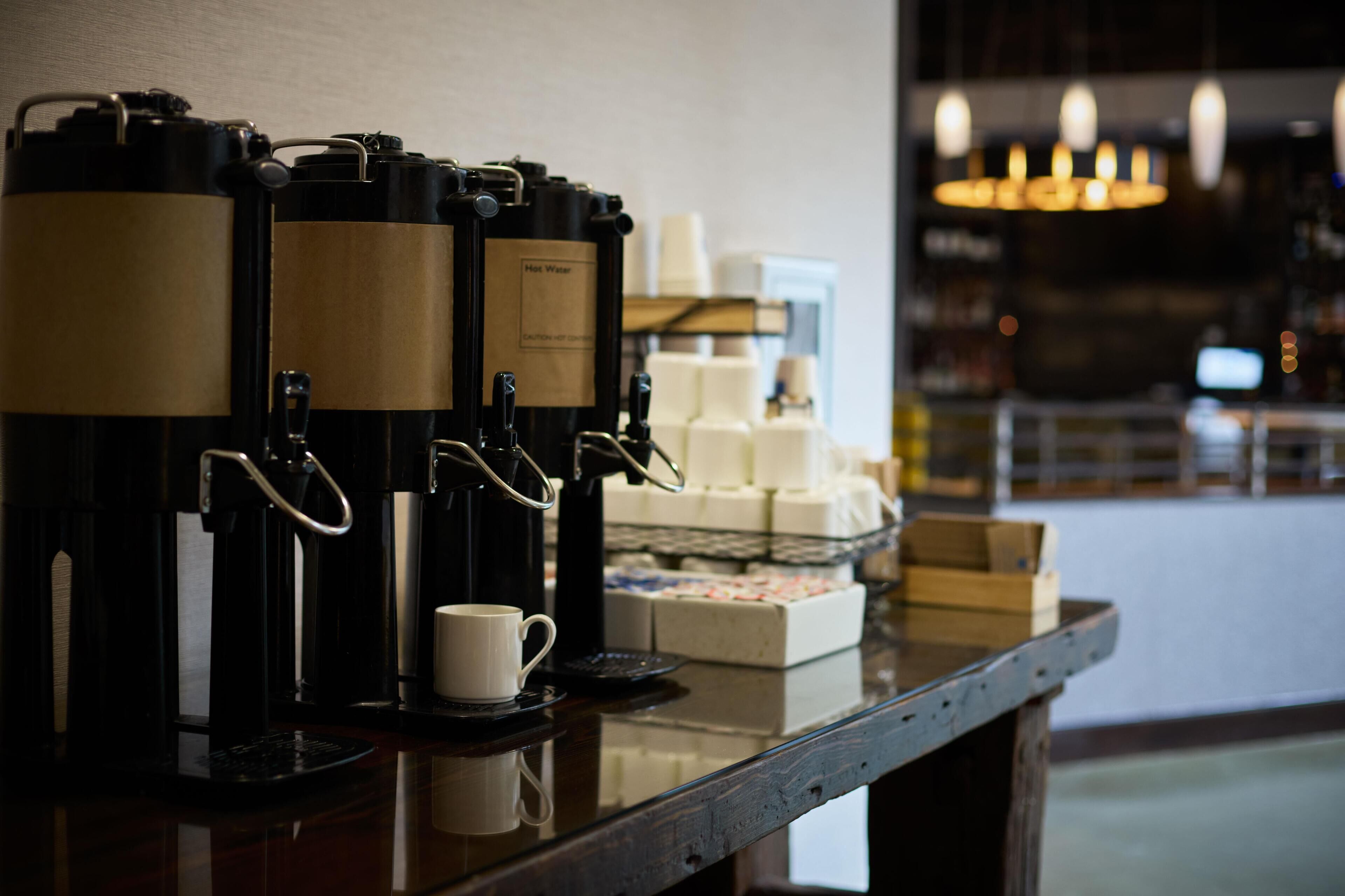 A coffee station with multiple espresso machines, a cup of coffee, and a display of pastries.