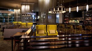Zona de bar moderna con asientos, luces colgantes y barra repleta de botellas.