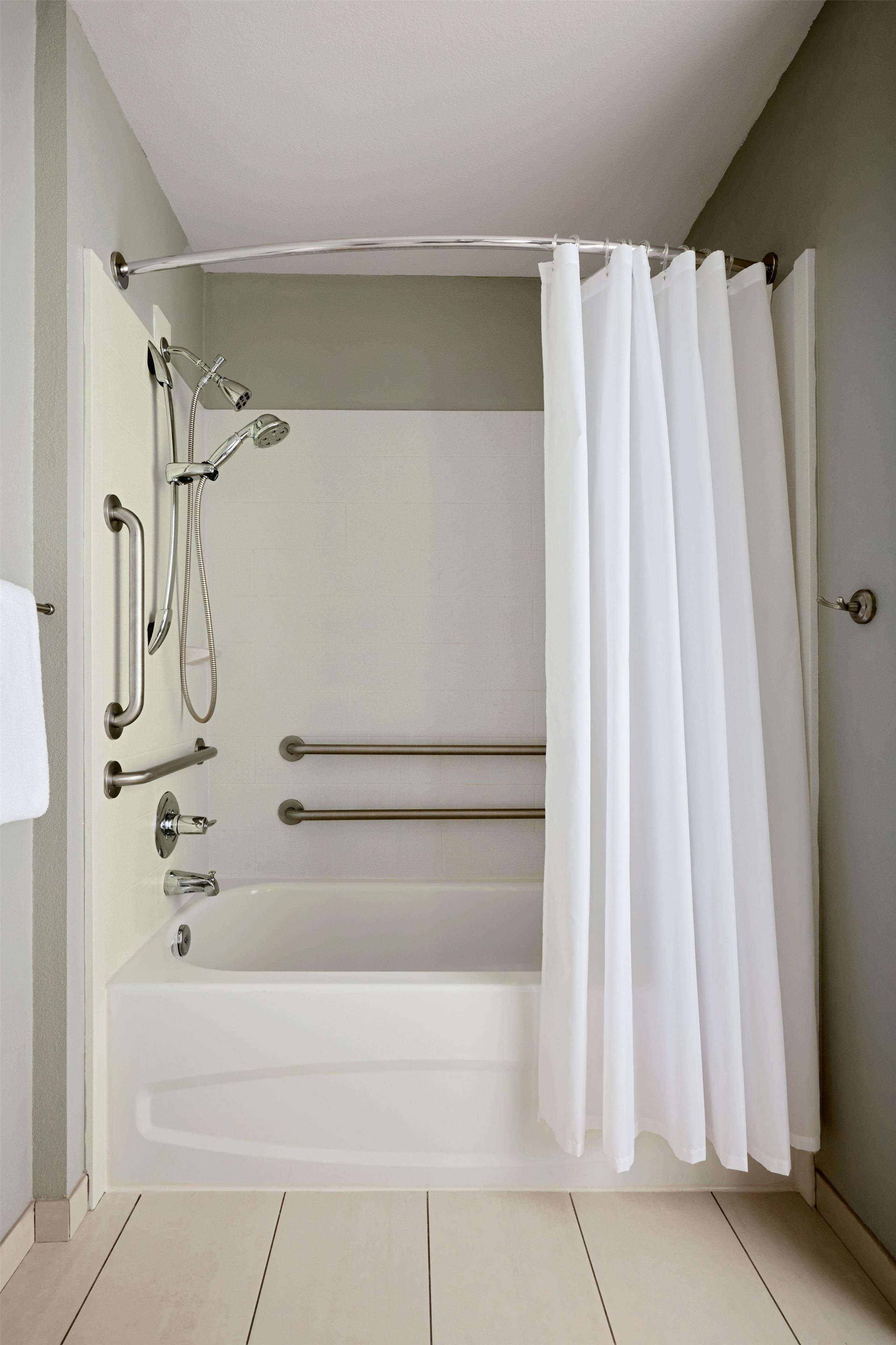 A modern bathroom with a bathtub, shower, and grab bars.