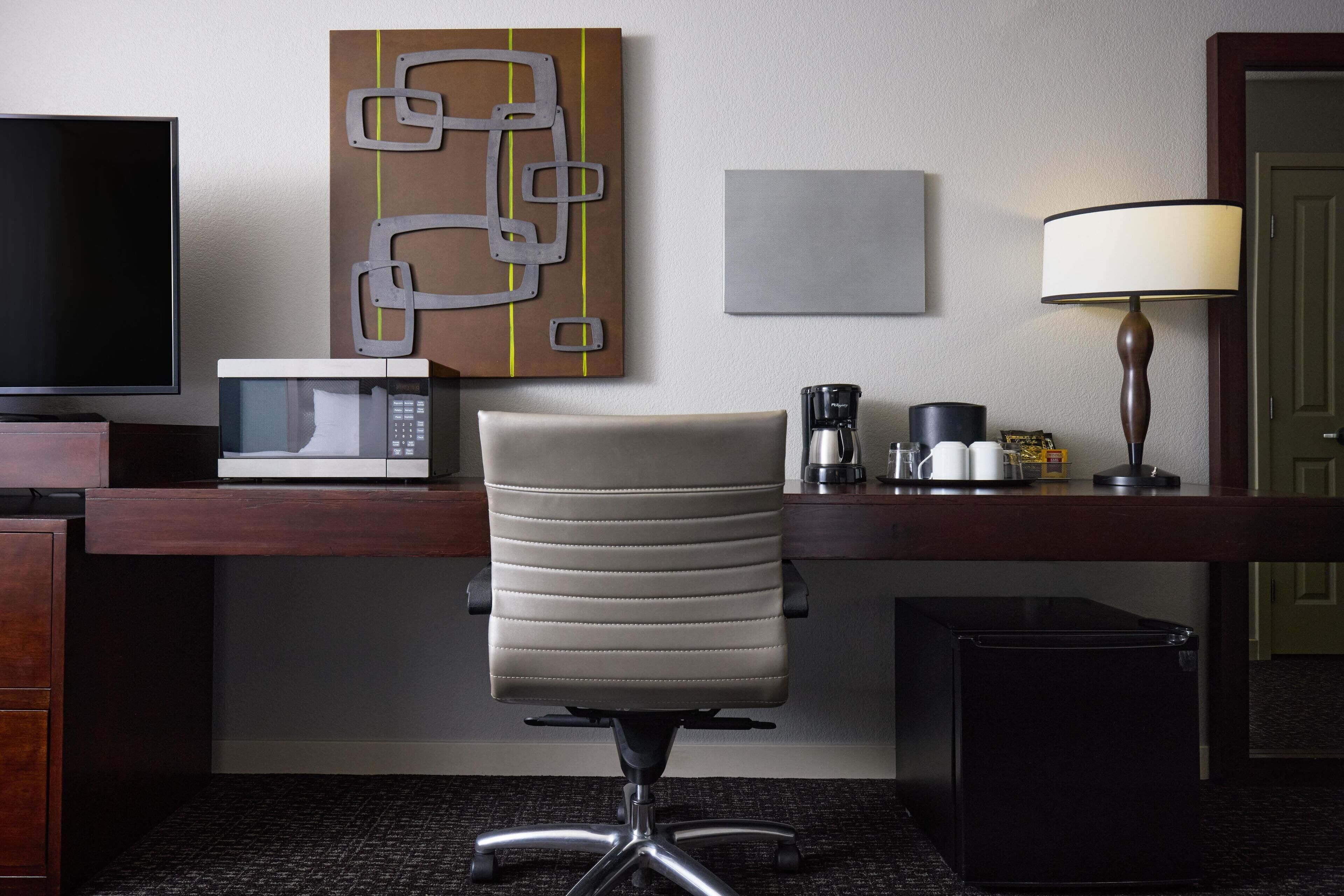 Une chambre d’hôtel équipée d’un bureau, d’une chaise, d’une télévision, d’un four à micro-ondes, d’une machine à café, d’une lampe et d’une poubelle.