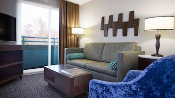 Une chambre d’hôtel équipée d’un canapé, d’un fauteuil, d’une télévision, d’une lampe et offrant une vue sur l’extérieur.