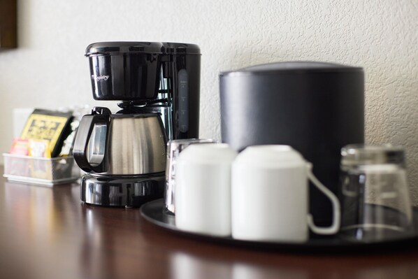 A coffee maker, two white cups, a salt and pepper shaker, and a small container with a price tag on a wooden table.