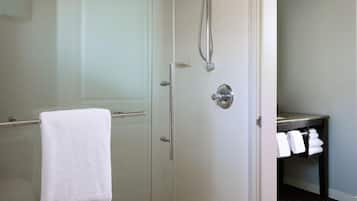 Un baño moderno con cabina de ducha de vidrio, una toalla blanca colgada en la puerta y un lavabo con toallas a la vista.