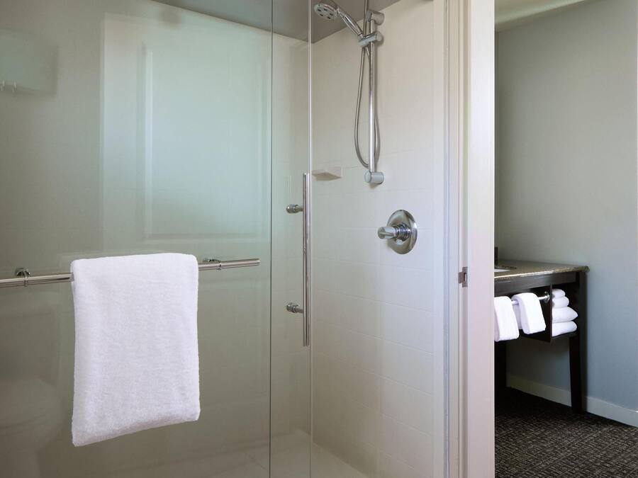 Un baño moderno con cabina de ducha de vidrio, una toalla blanca colgada en la puerta y un lavabo con toallas a la vista.