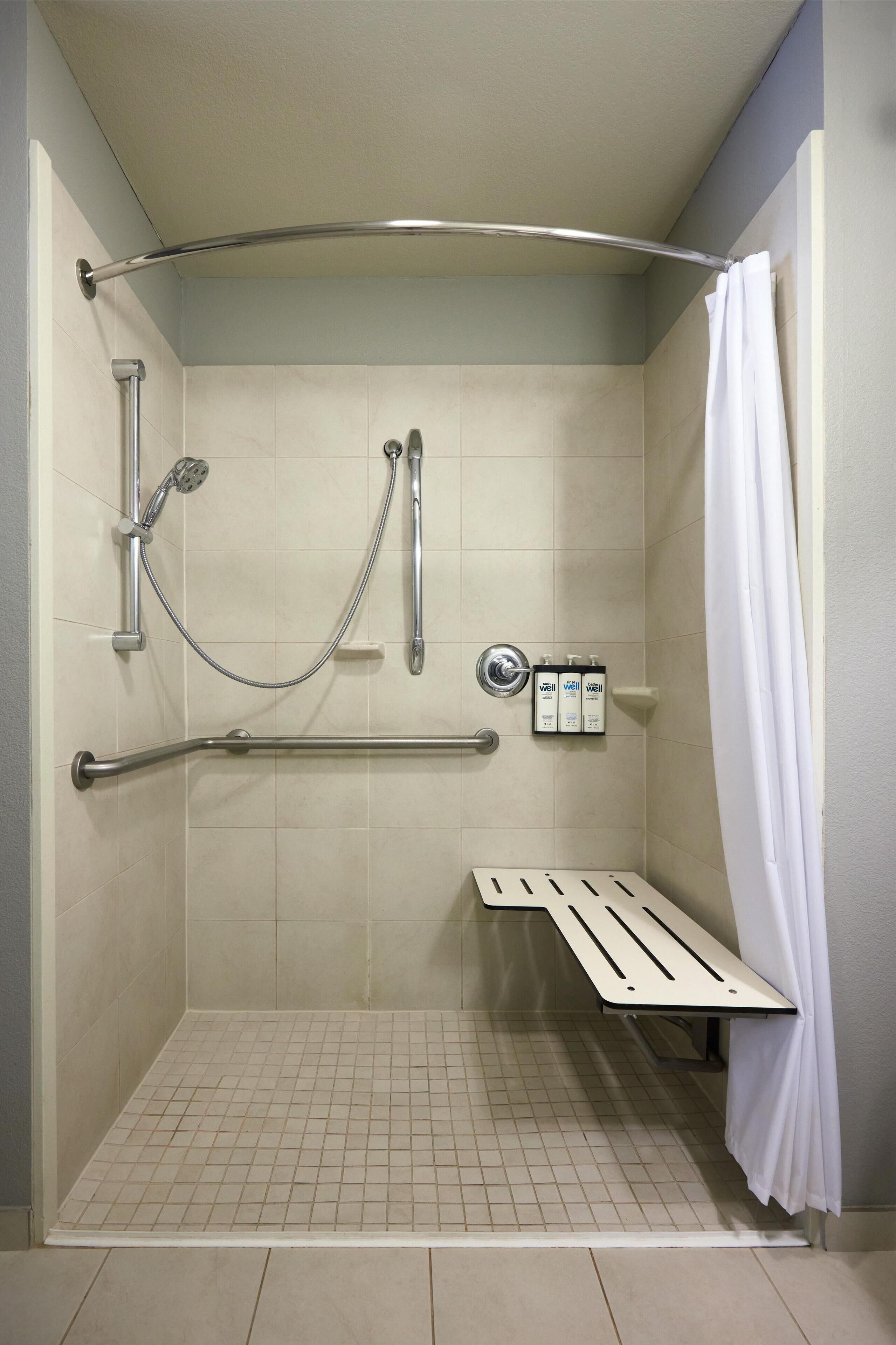 A shower stall with grab bars, a bench, and a showerhead.