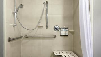 A shower stall with grab bars, a bench, and a showerhead.