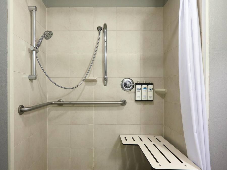 Un box de ducha con barras de apoyo, un asiento y un cabezal de ducha.