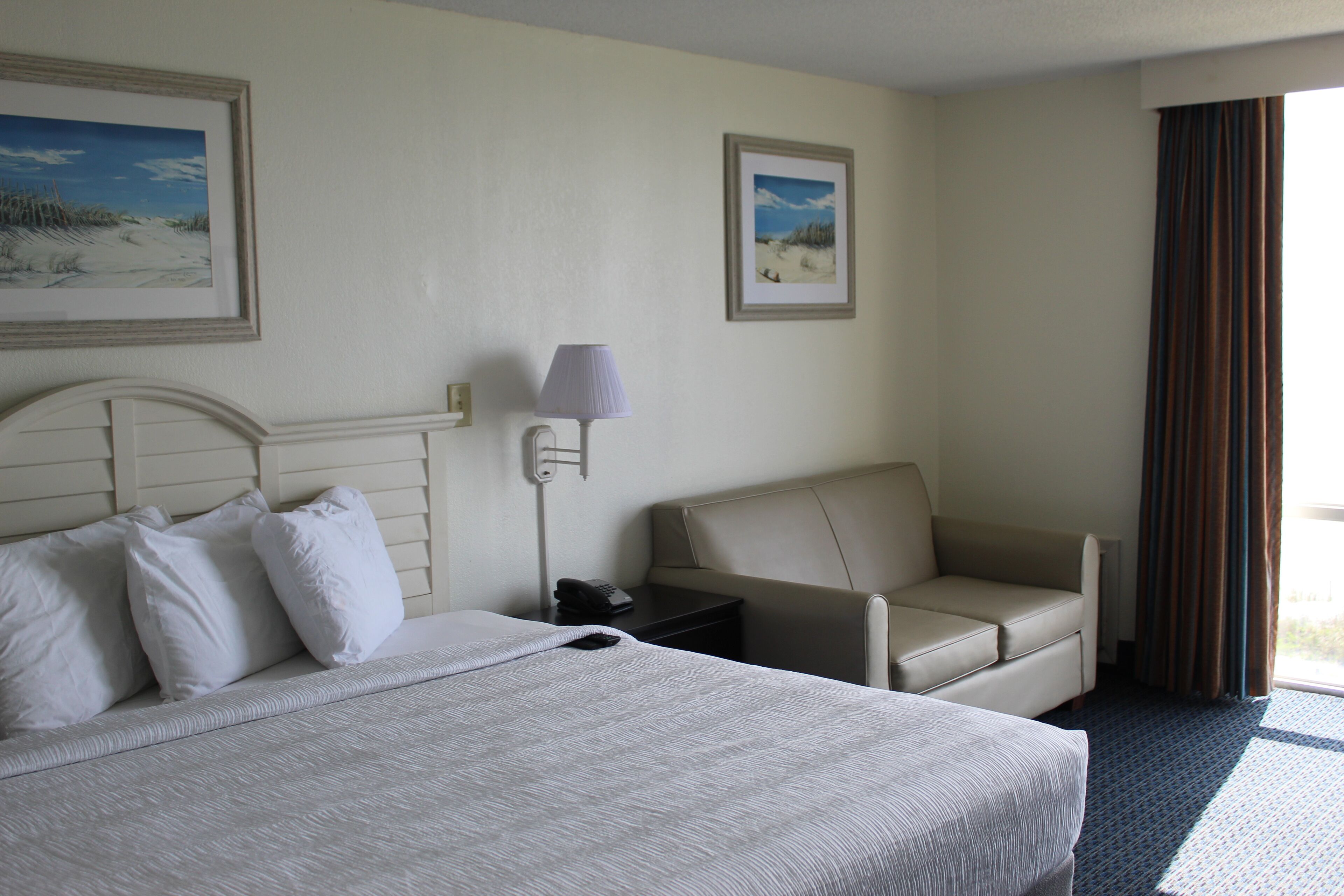 A hotel room with a large bed, a sofa, a nightstand, and two framed pictures on the wall.