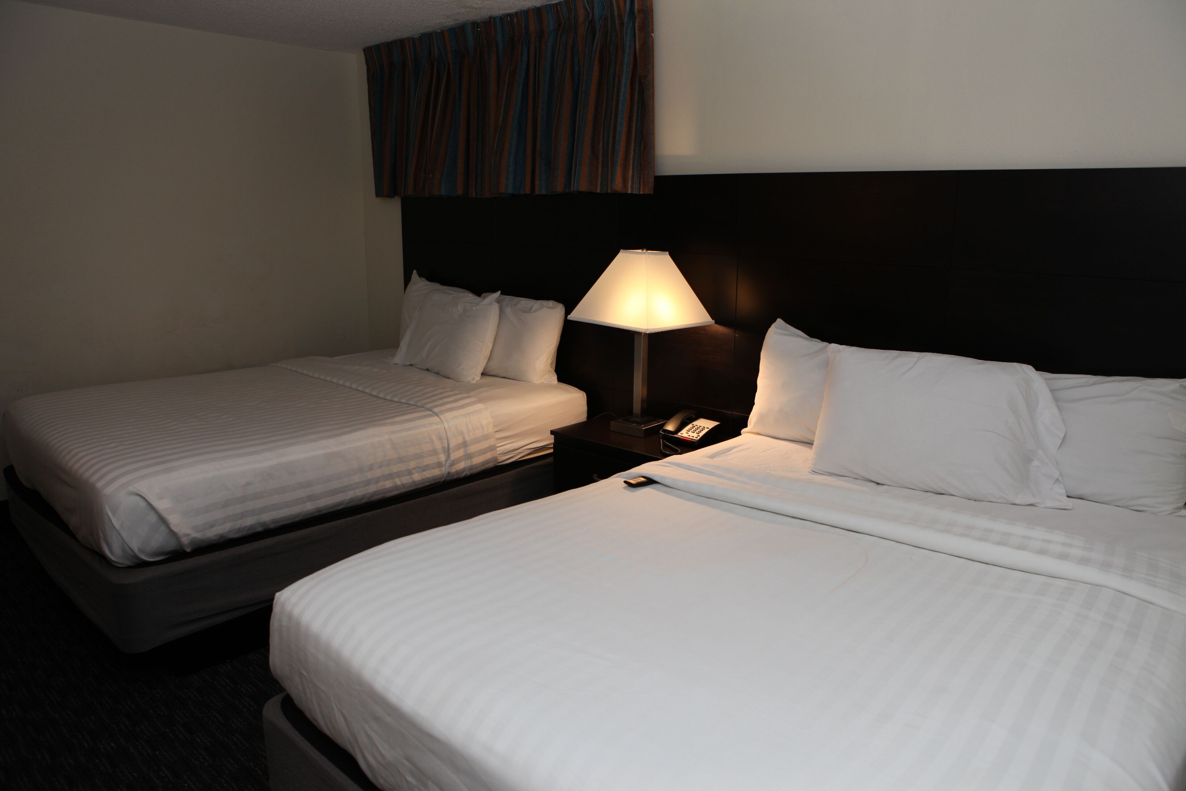 Een hotelkamer met twee enkele bedden, een nachtkastje met een lamp en een gestreept gordijn.