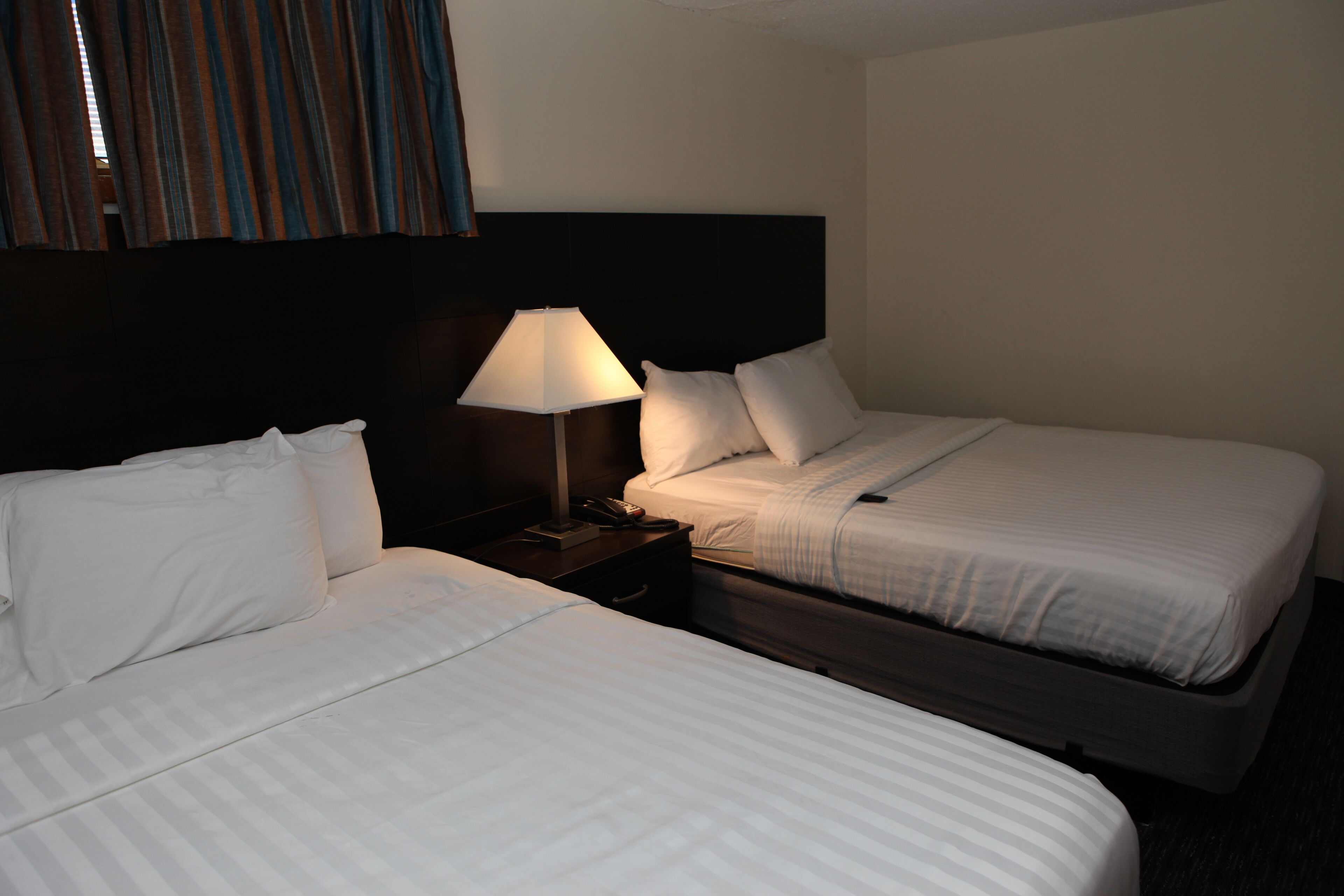 A hotel room with two beds, a nightstand with a lamp, and a headboard.