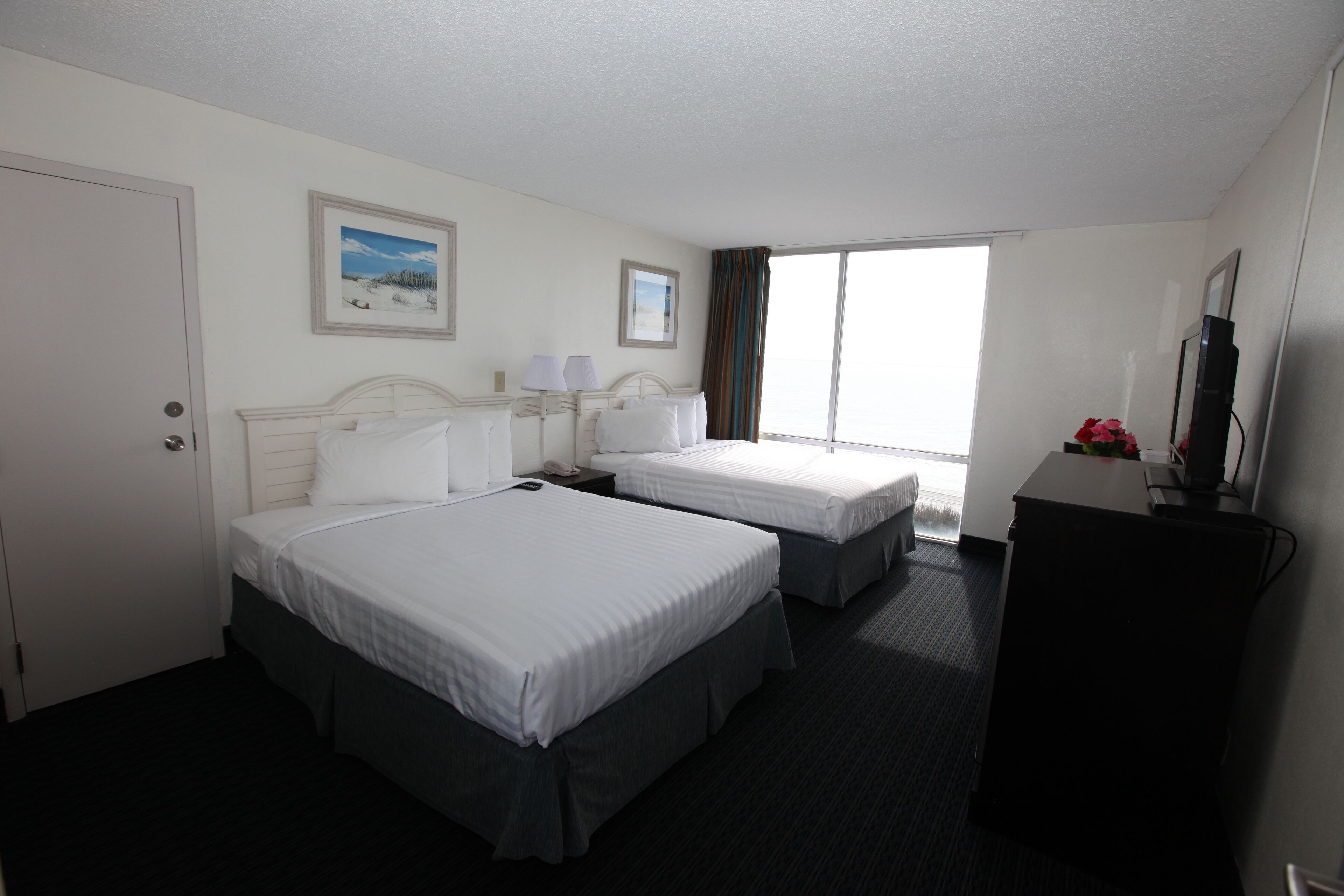 A hotel room with two beds, a desk, a TV, and a window with curtains.