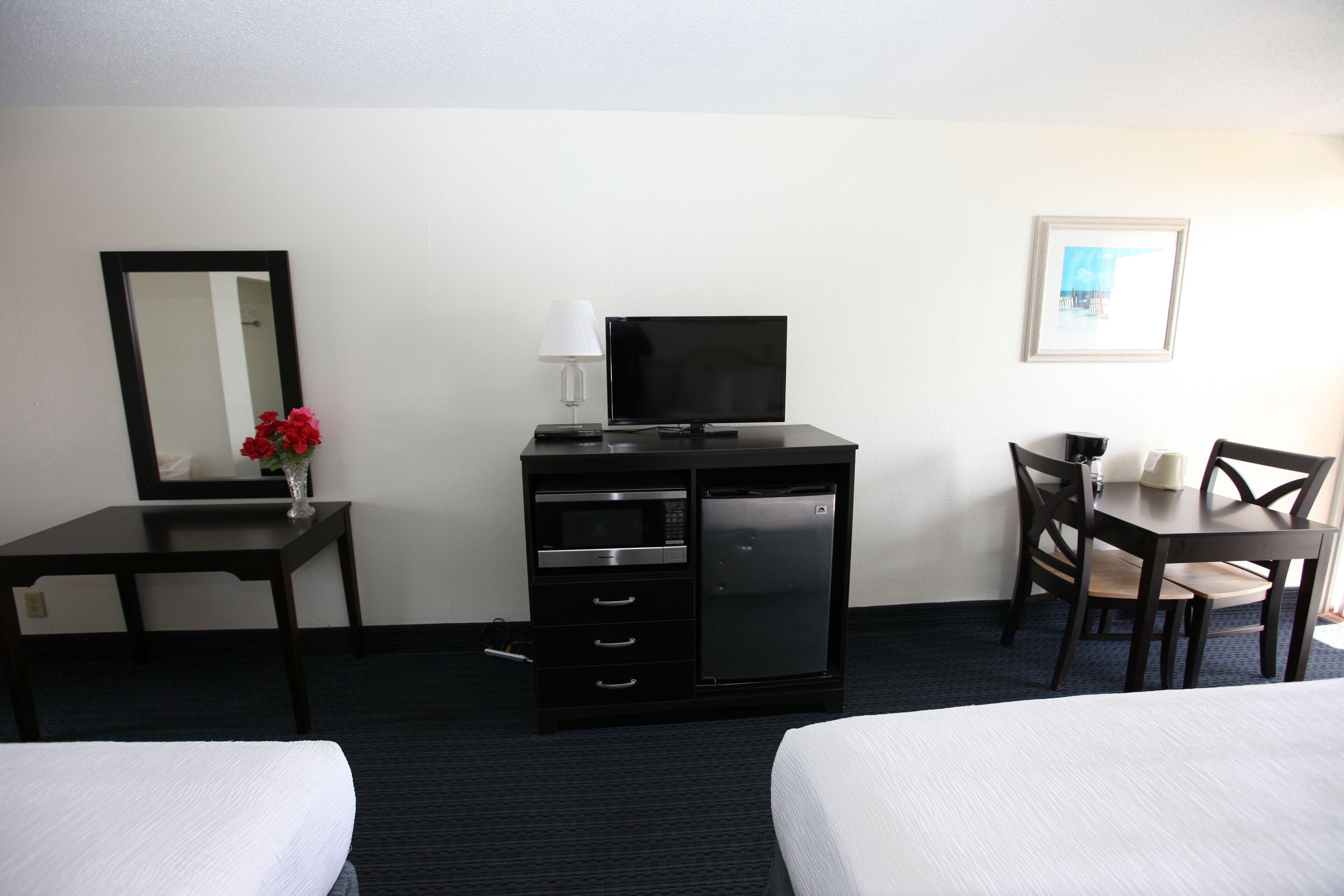 A hotel room with a bed, a desk with a computer, a microwave, and a refrigerator.