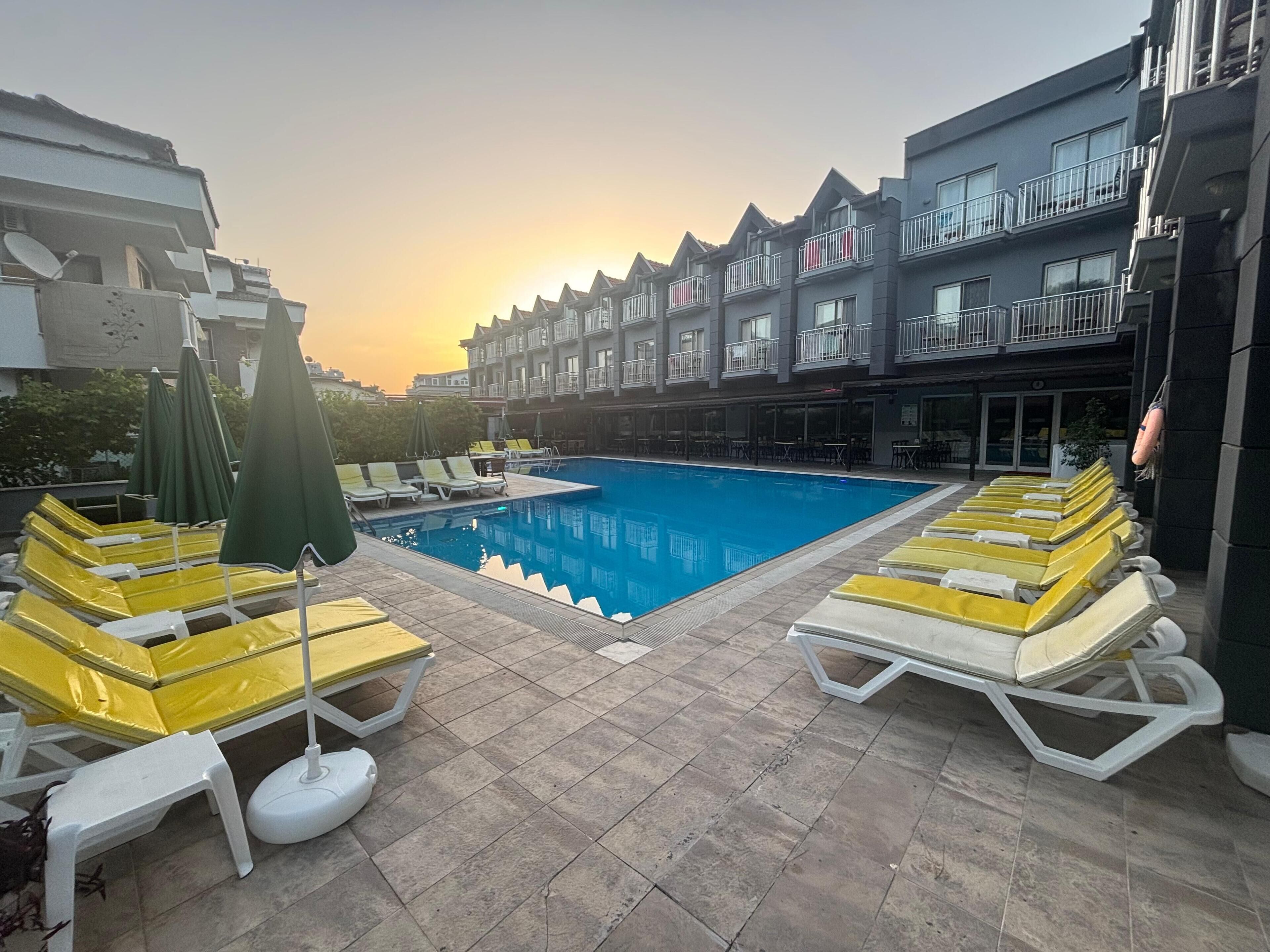 A swimming pool with sun loungers and umbrellas, surrounded by a building with balconies.