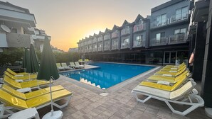 Una piscina con tumbonas y sombrillas, rodeada por un edificio con balcones.