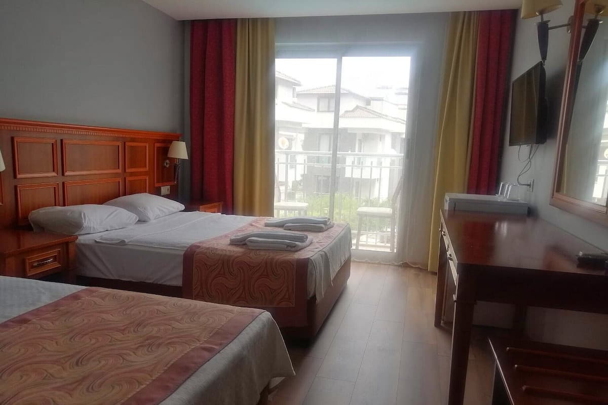 Une chambre d’hôtel avec deux lits, une tête de lit en bois, un bureau, une télévision et un balcon donnant sur des immeubles.