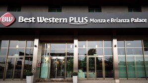Een hotelentree met grote glazen deuren, een bord met de tekst 'Best Western PLUS Monza e Brianza Palace' en een stoep van rode bakstenen ervoor.