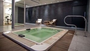 Een modern wellnessruimte met een jacuzzi, houten vloeren en fitnessapparatuur op de achtergrond.