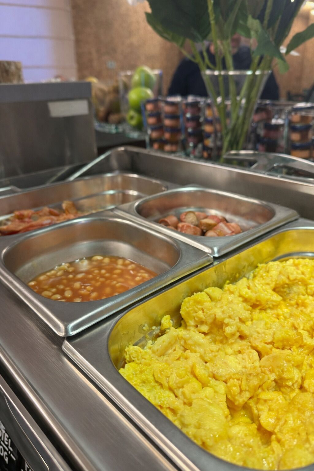 Ein Buffet mit verschiedenen Speisen, darunter Bohnen, Würstchen und Rührei.