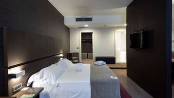 A modern hotel room with a large bed, bedside tables, a flat-screen TV, and a walk-in closet.
