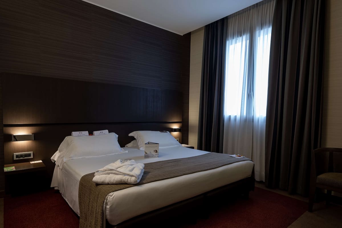 Een hotelkamer met een groot bed, een nachtkastje, een stoel en een raam met gordijnen.