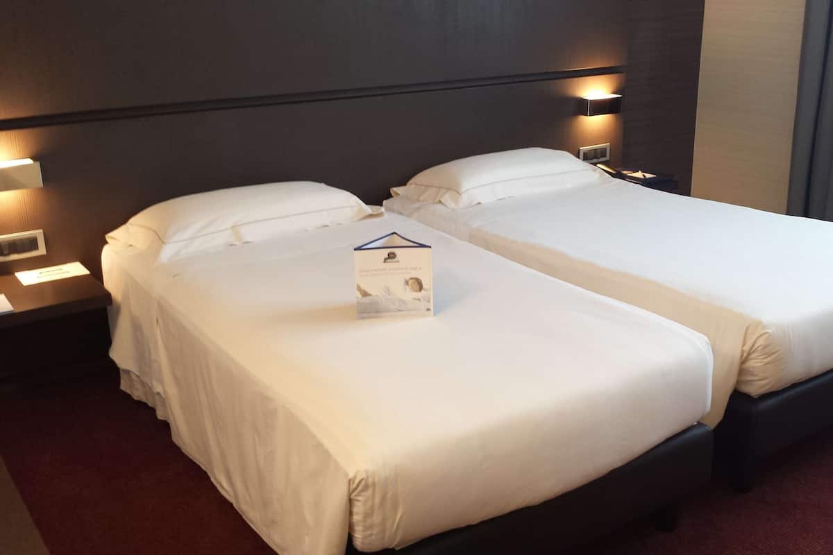 Een hotelkamer met twee enkele bedden, een nachtkastje met een lamp en een klein tafeltje met schrijfschrift.