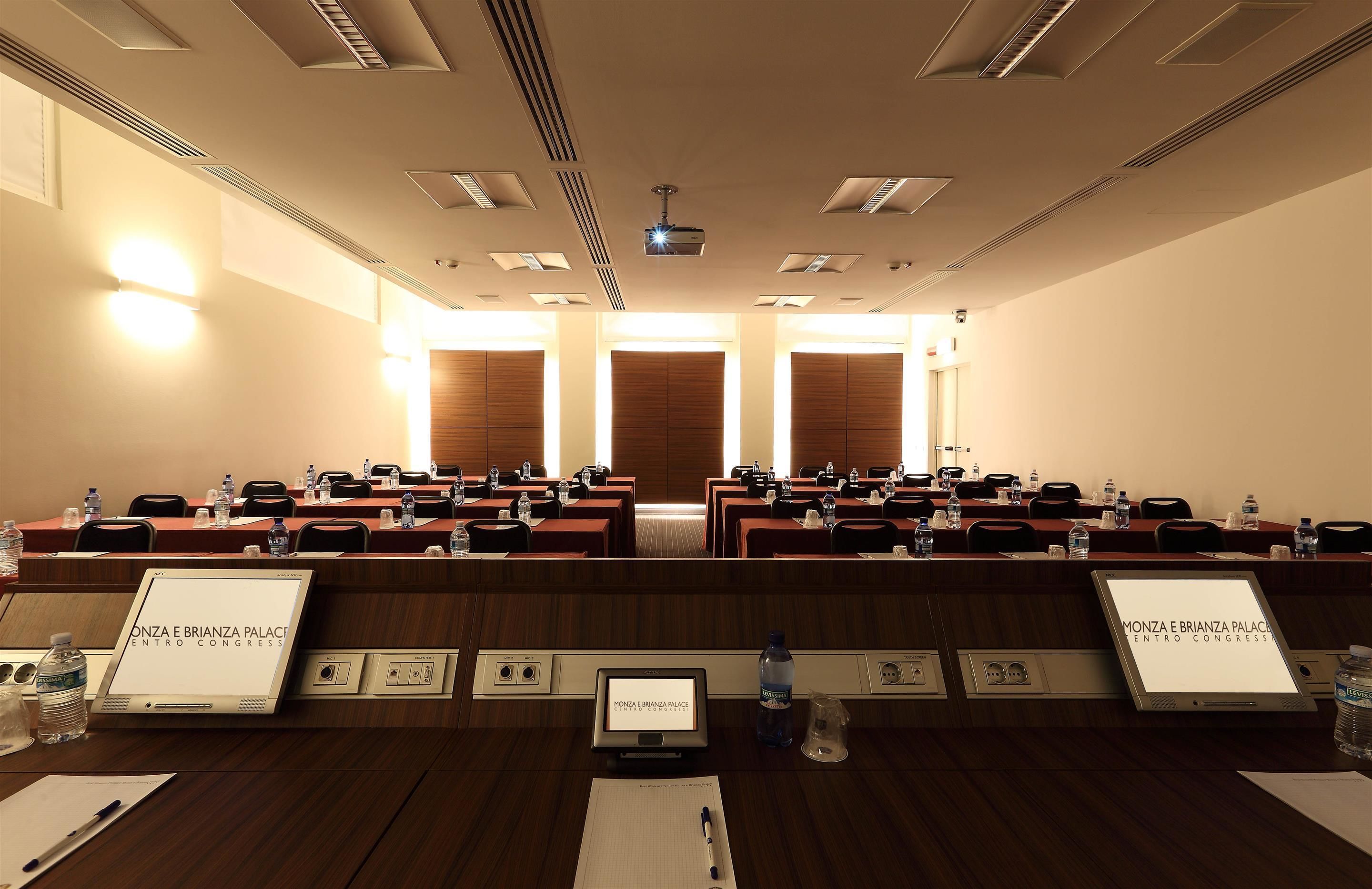 A conference room with rows of tables and chairs, nameplates, water bottles, and a projector on the ceiling.