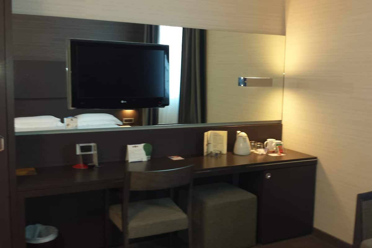 Een hotelkamer met een donker houten bureau, een stoel, een televisie boven het bureau en een kleine spiegel.