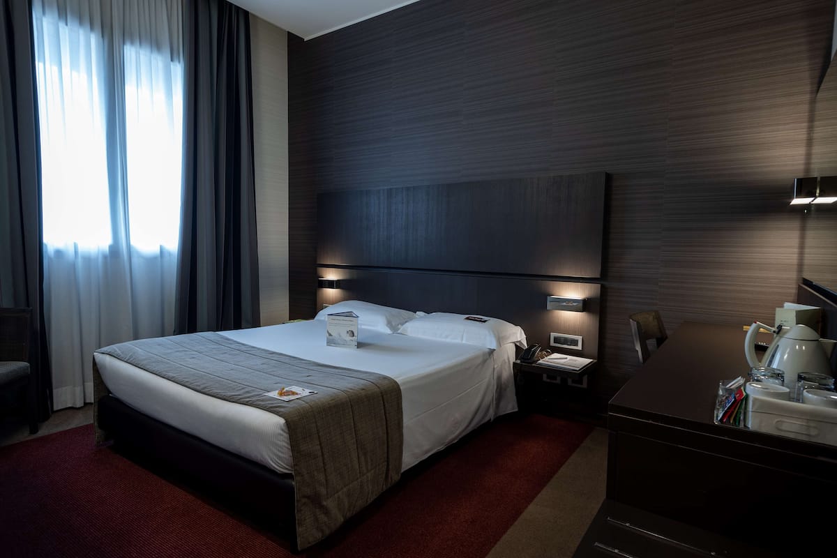 Een hotelkamer met een groot bed, nachtkastjes met lampen, een bureau met stoel en een koffiezetapparaat.