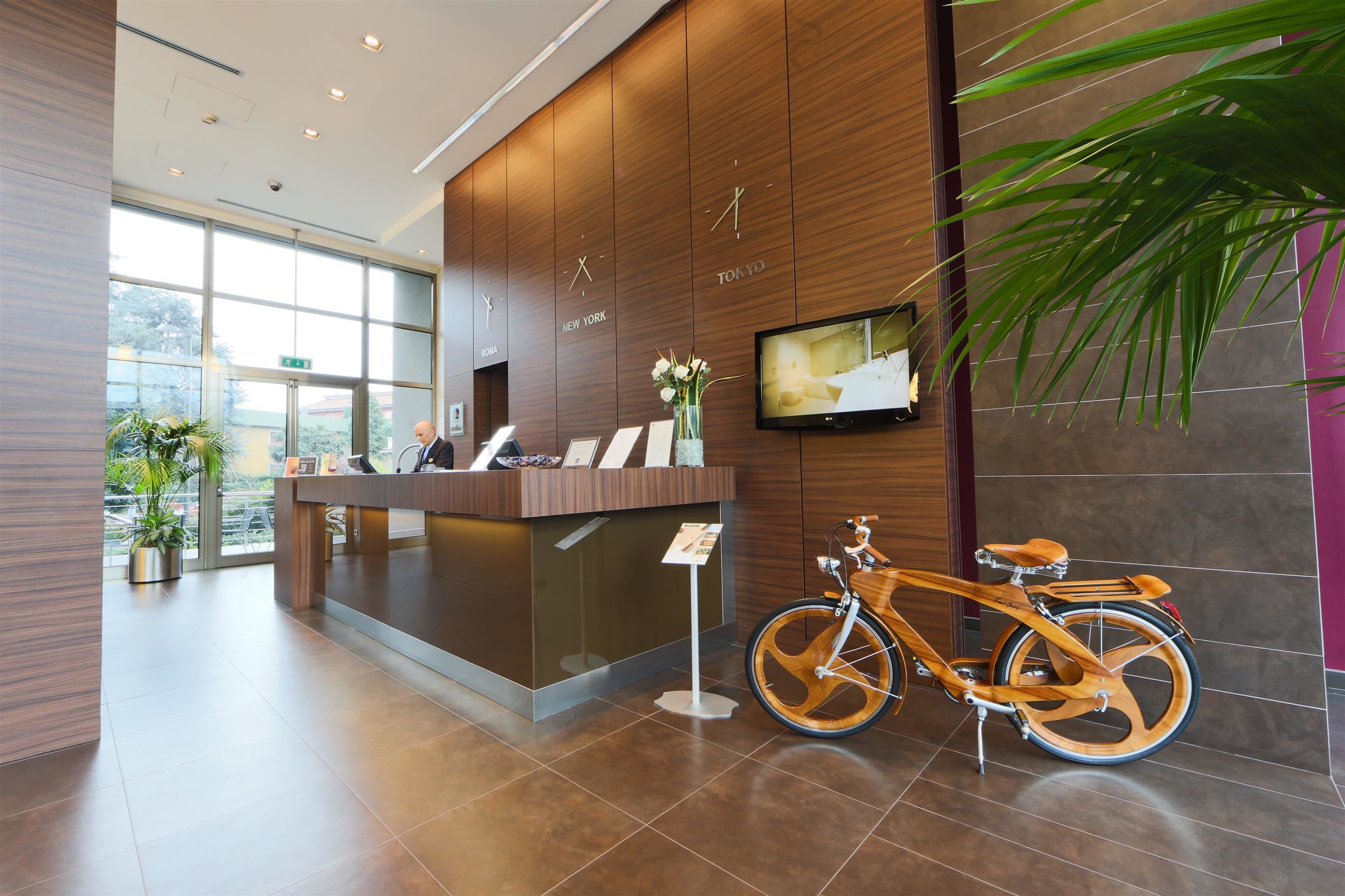 A modern reception area with a wooden reception desk, a television mounted on the wall, and a bicycle parked to the side.