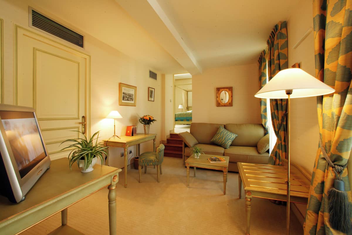 A living room with a sofa, coffee table, and a lamp. There is a door, a plant, and a picture frame on a table.