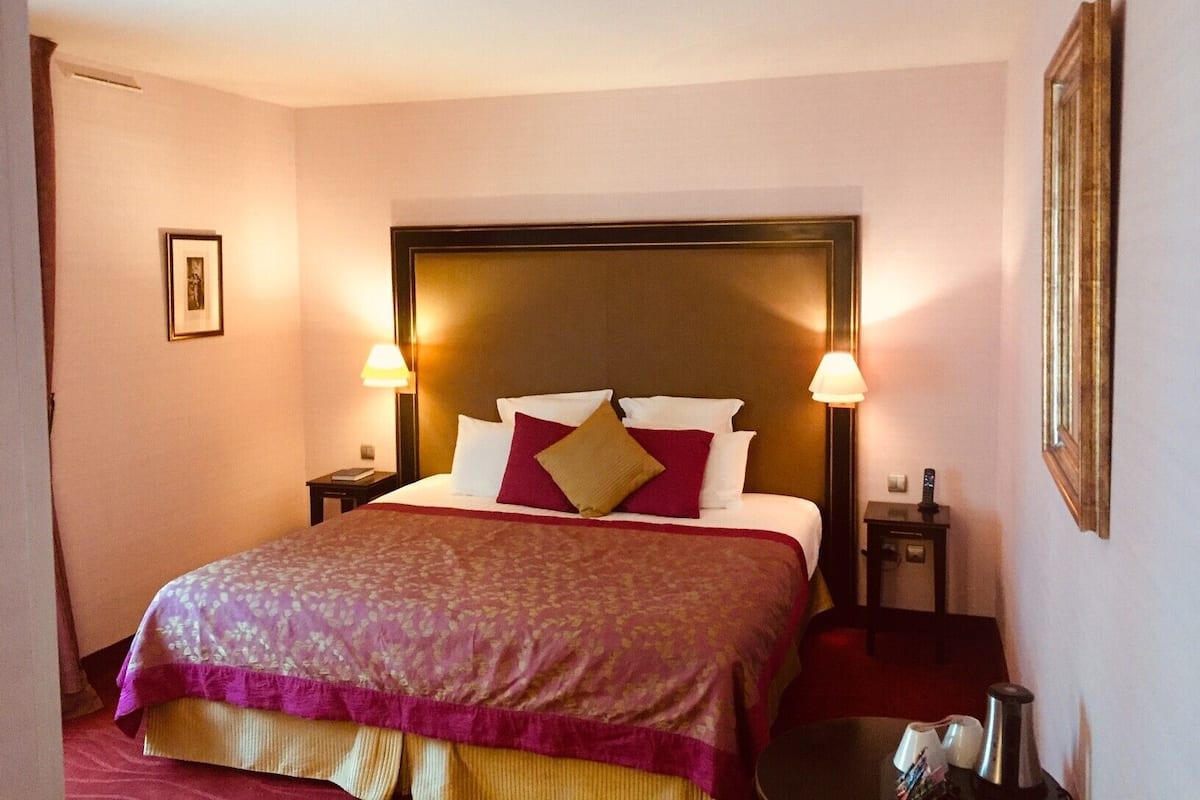 A hotel room with a large bed, two bedside tables, a nightstand, and a framed picture on the wall.