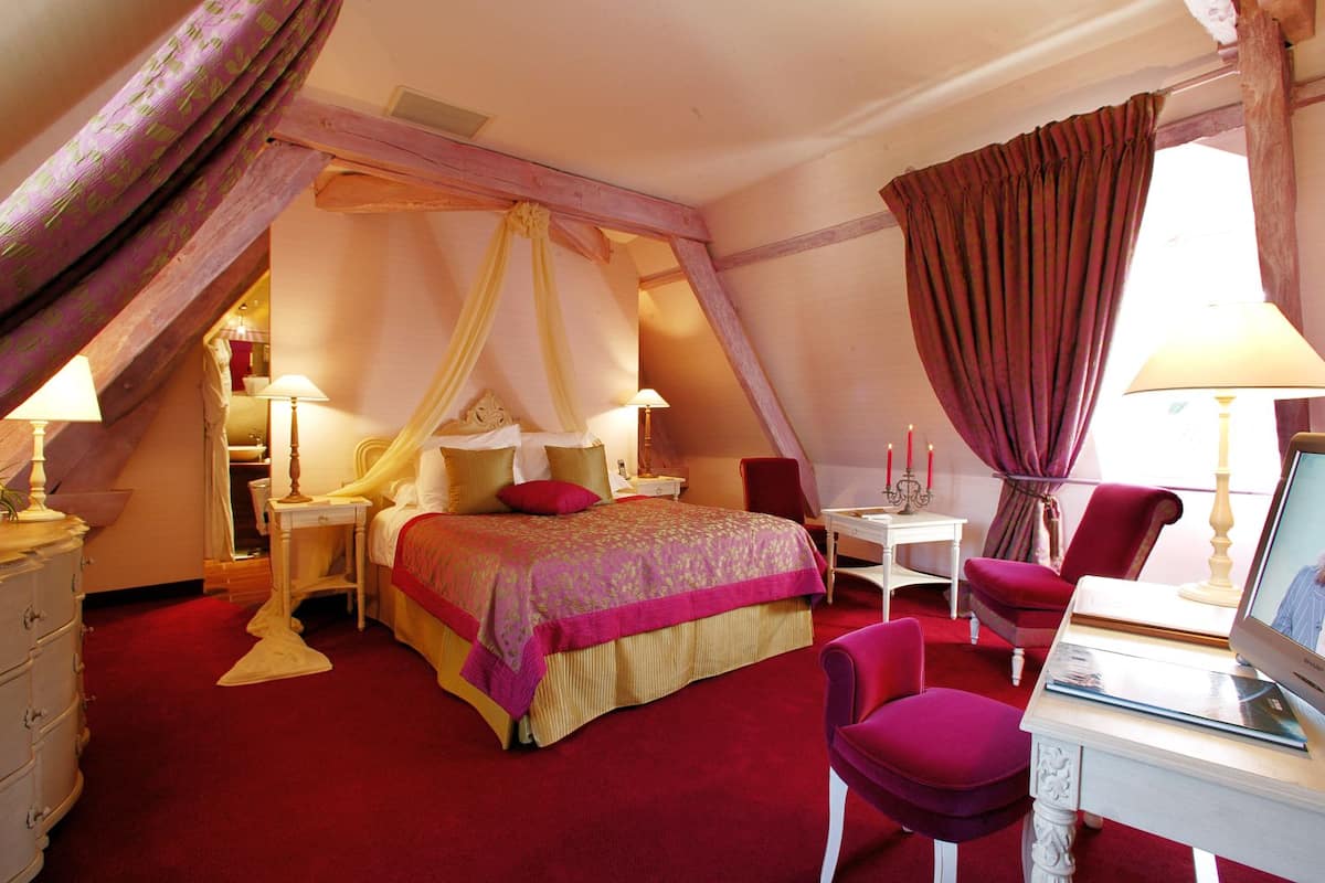 A bedroom with a bed, a desk, a chair, a TV, and a red carpet.