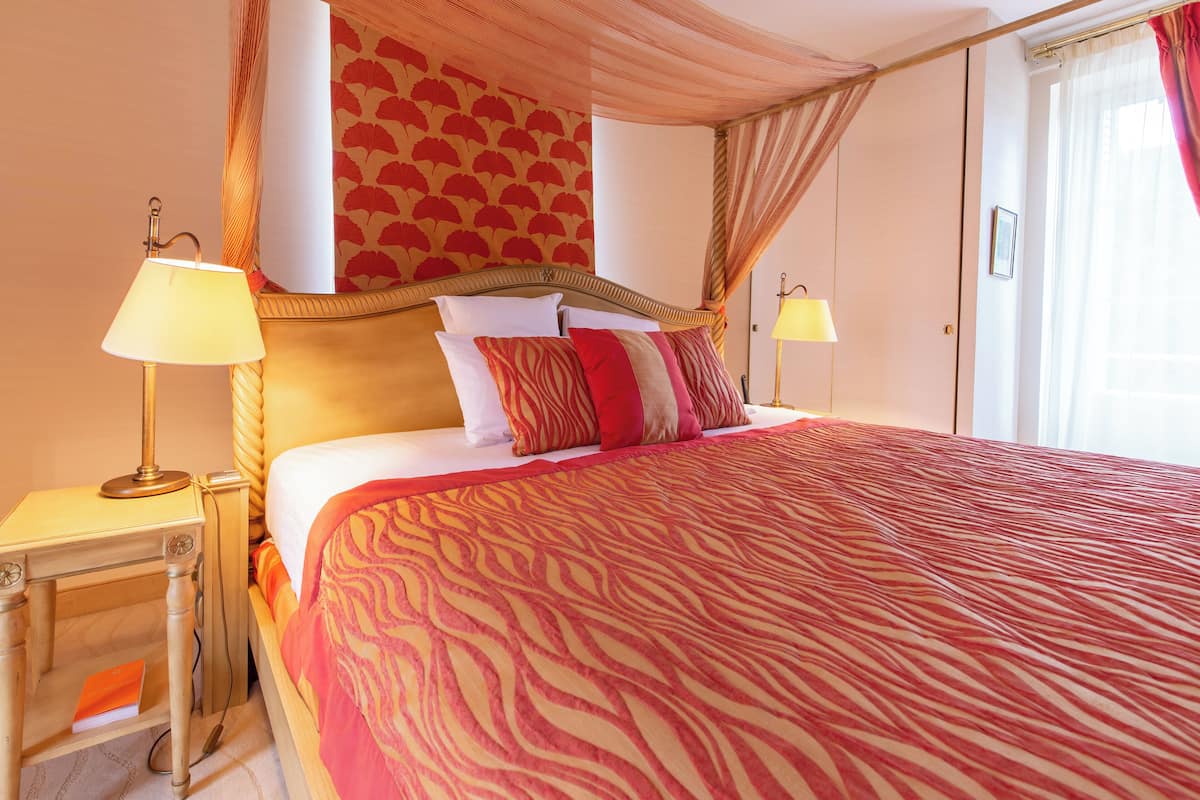 A hotel room with a large bed, two bedside lamps, a nightstand, and a window with curtains.