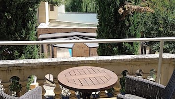 A balcony with wicker furniture and a table, overlooking a building and greenery.