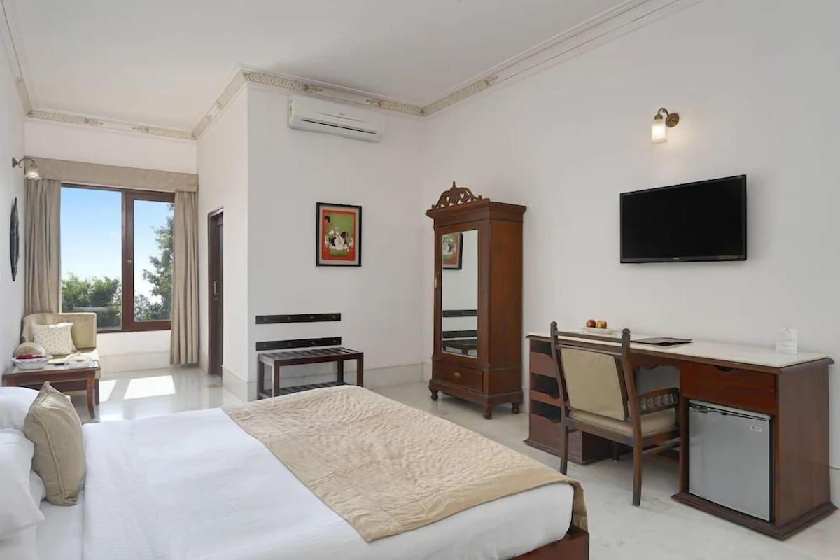 A hotel room with a bed, desk, chair, TV, wardrobe, and a window.
