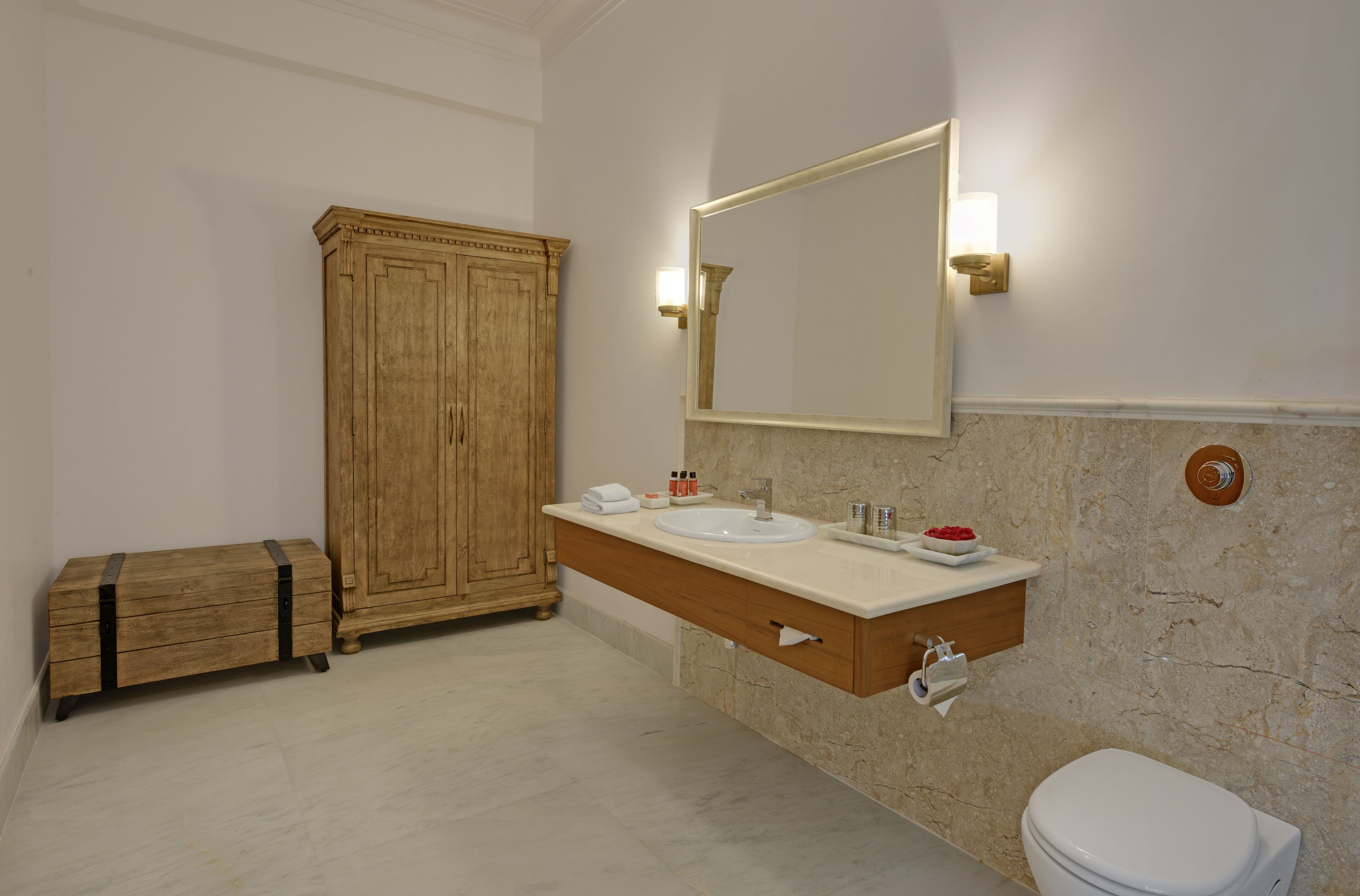 Un baño con un mueble de madera, un espejo grande, un lavabo con encimera de mármol y un inodoro.