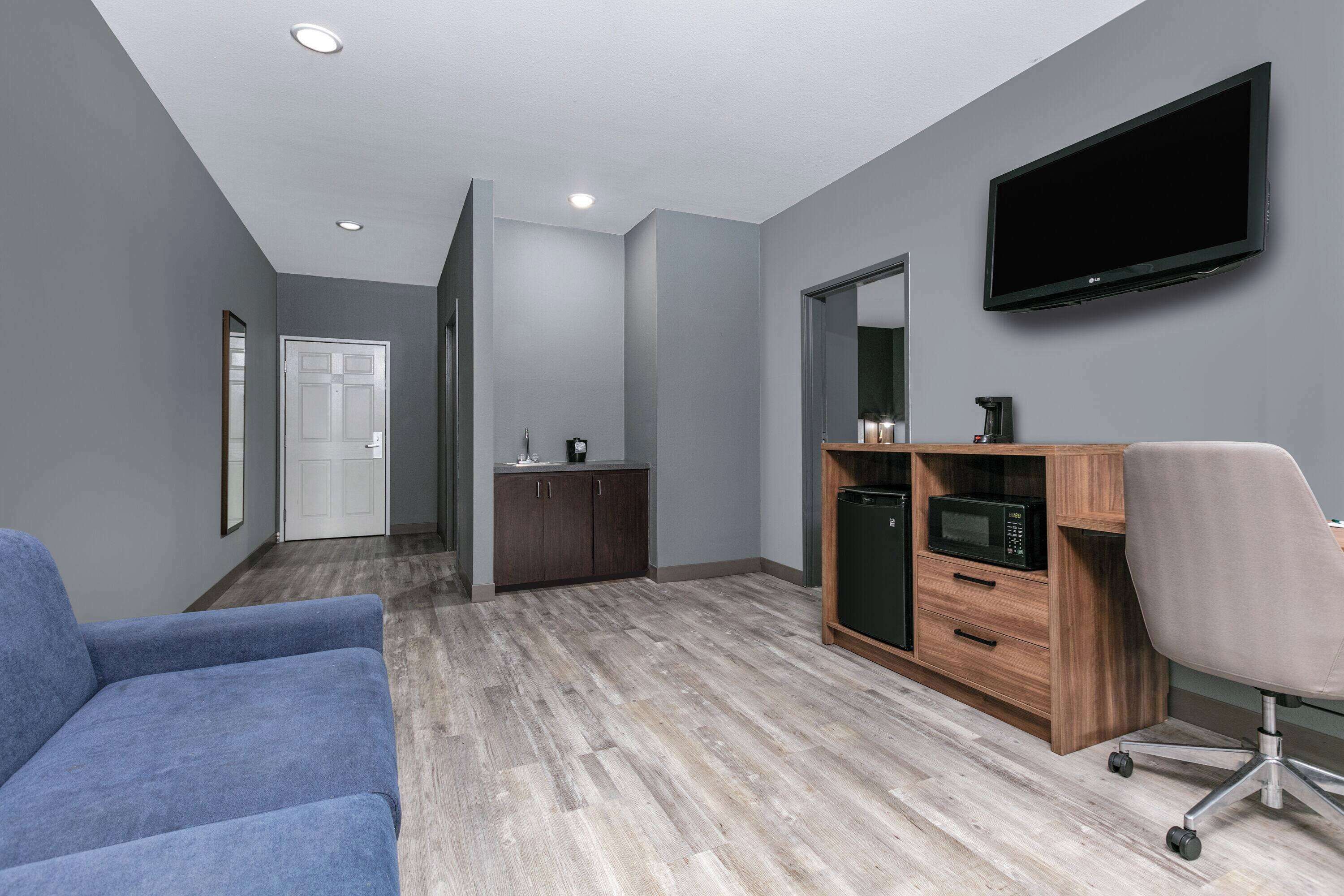 A modern room with a sofa, kitchenette, and a TV mounted on the wall.