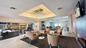 A modern hotel lobby with a reception desk, seating area, and a dining section.