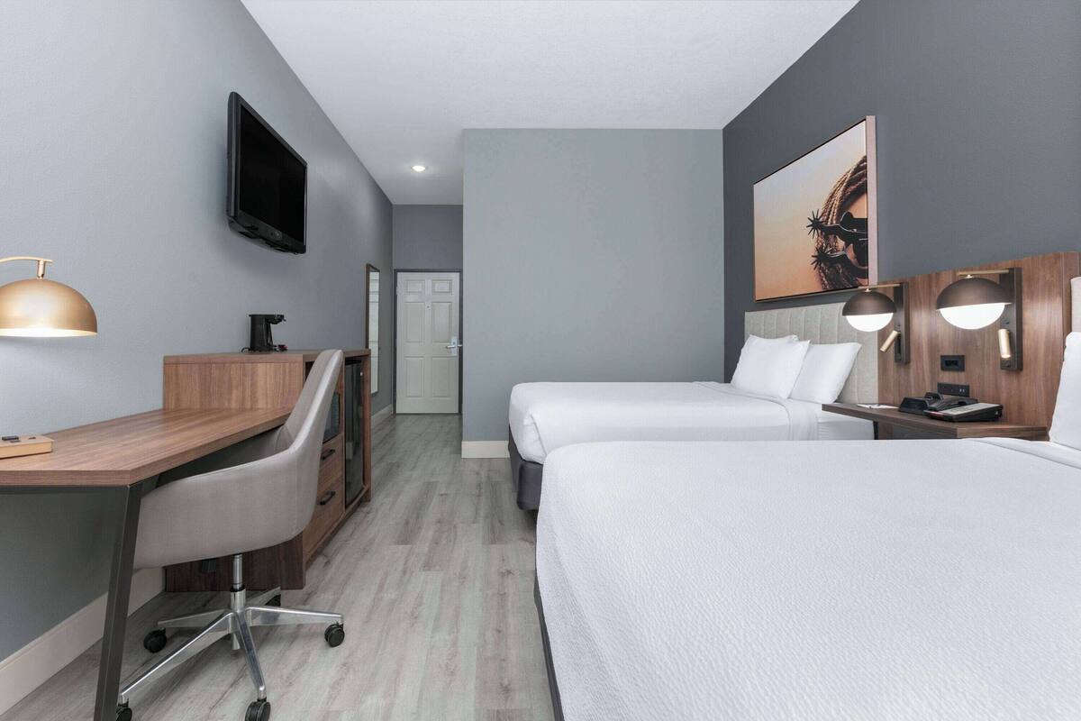 Une chambre d’hôtel moderne équipée d’un bureau, de deux lits, d’une télévision et d’un tableau au mur.