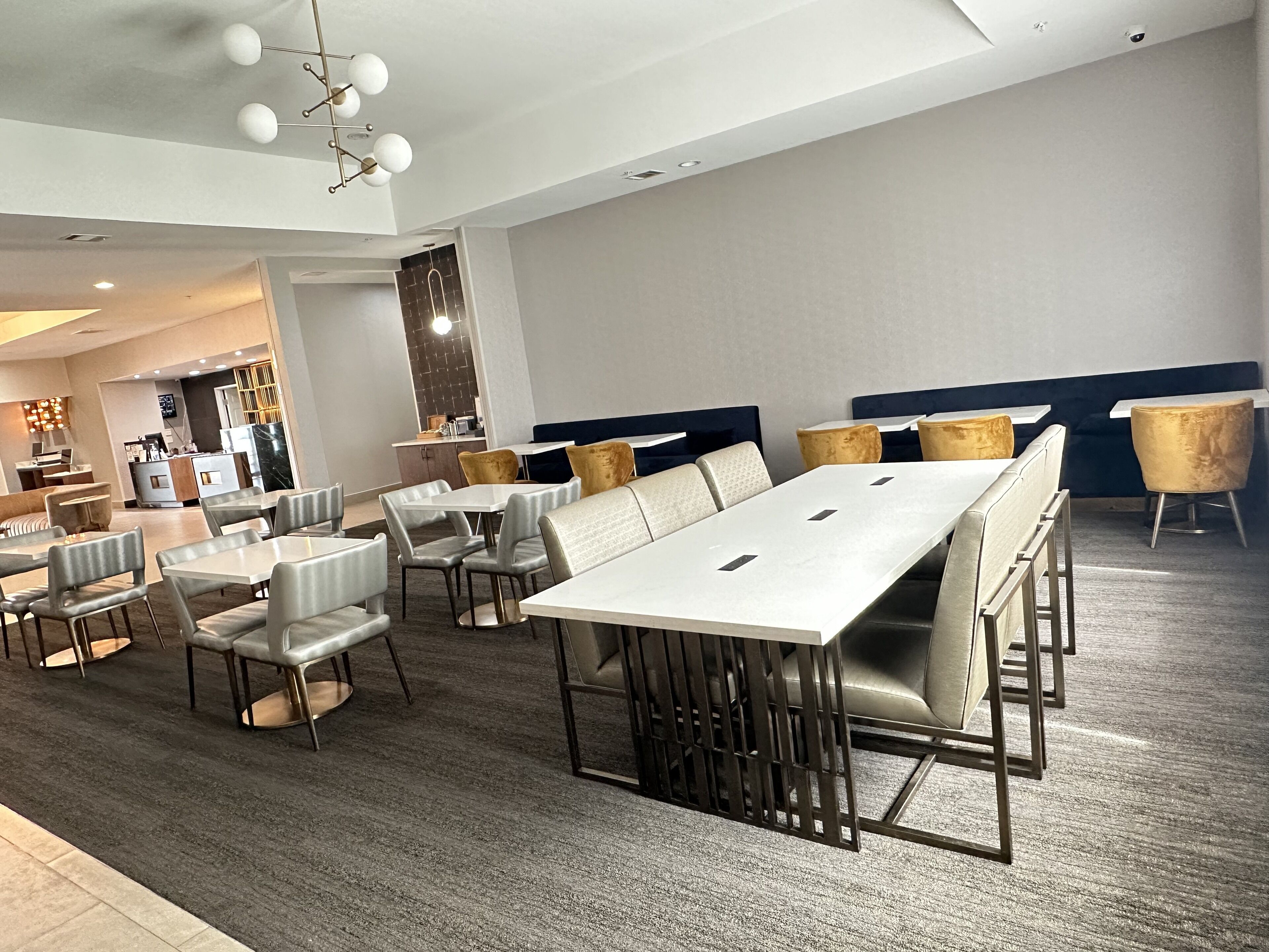 Un'area ristorazione moderna con tavoli e sedie bianche, un angolo bar con bancone e un'area salotto con panche imbottite.