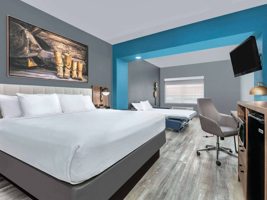 A modern hotel room with a large bed, a desk with a computer, a chair, and a television.