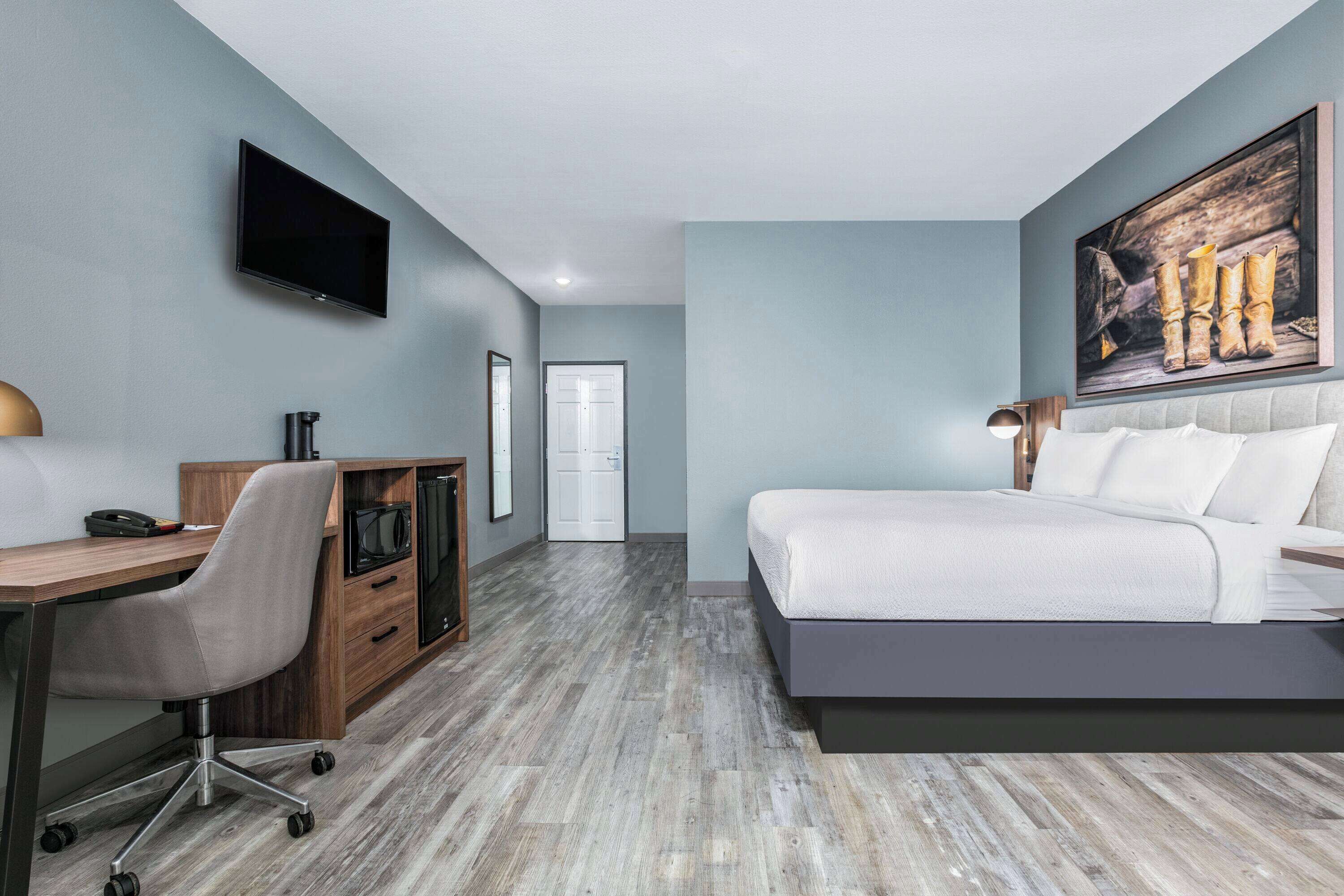 Una habitación de hotel moderna con una cama grande, un escritorio con una silla, un televisor de pantalla plana en la pared y un cuadro sobre la cama.