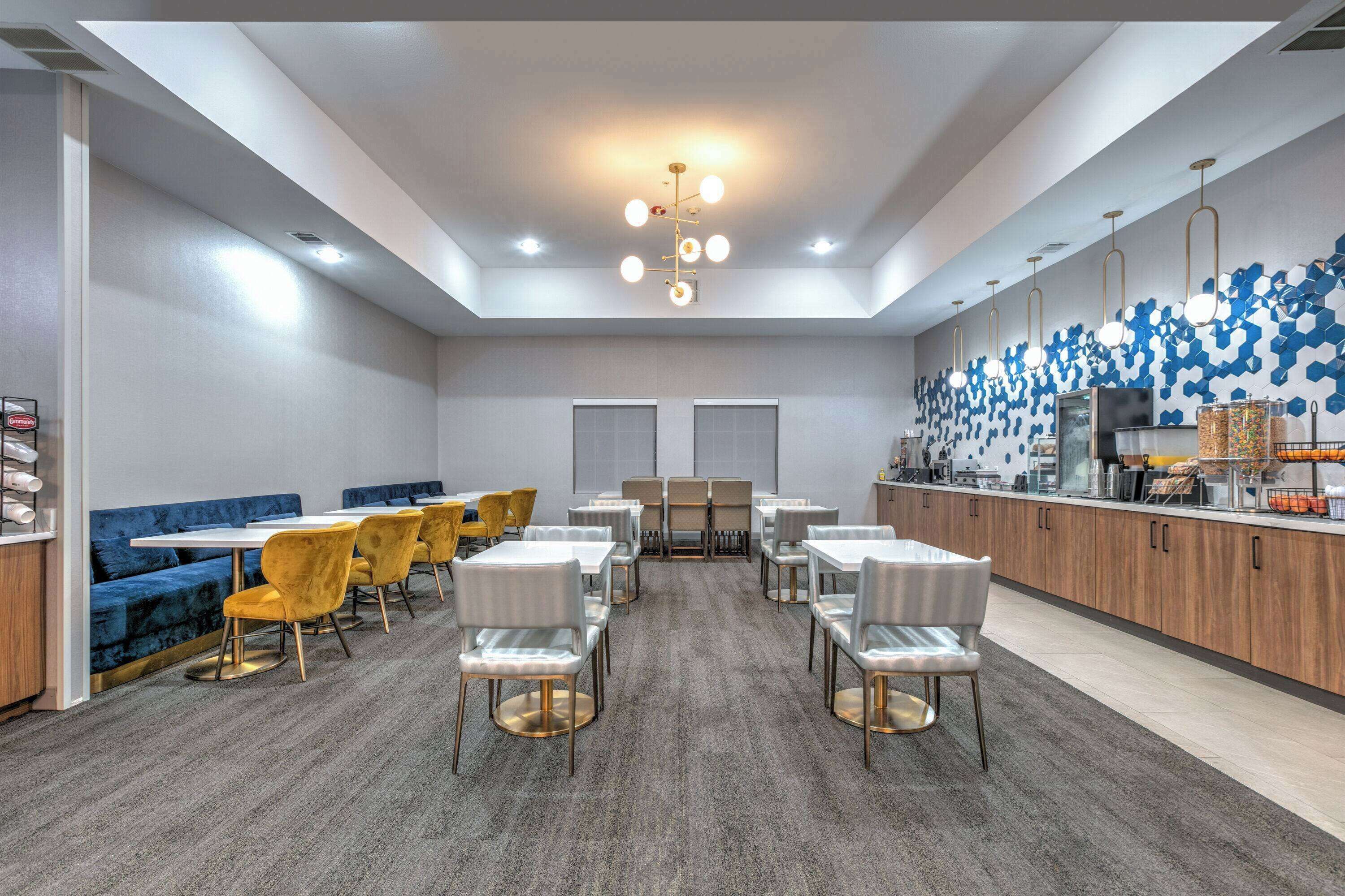 Un comedor moderno con una mesa central, rodeada de sillas, y una zona de estar azul en un lateral.