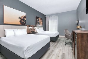 A hotel room with two beds, a desk, and a chair.