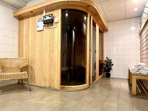 Una sauna de madera con puerta de cristal, una silla de mimbre y una mesa con toallas.