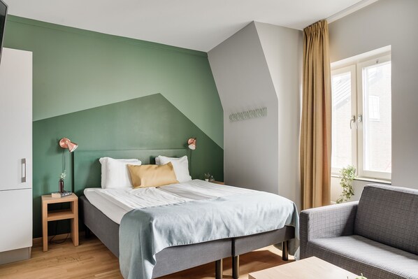A modern bedroom with a bed, bedside table, and a sofa. - The Nooq Lund (Lund)