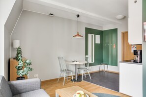 Una sala de estar moderna con un sofá, una mesa de centro con fruta, una zona de comedor con sillas, una lámpara colgante y una pared verde de acento.