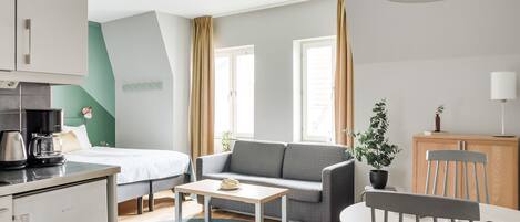 Una habitación de hotel moderna con cama, sofá, mesa de comedor y kitchenette.
