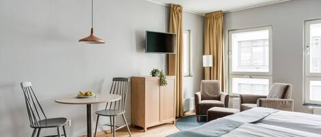 Habitación de hotel con cama, dos sillas, una mesita, televisor y ventana con cortinas.
